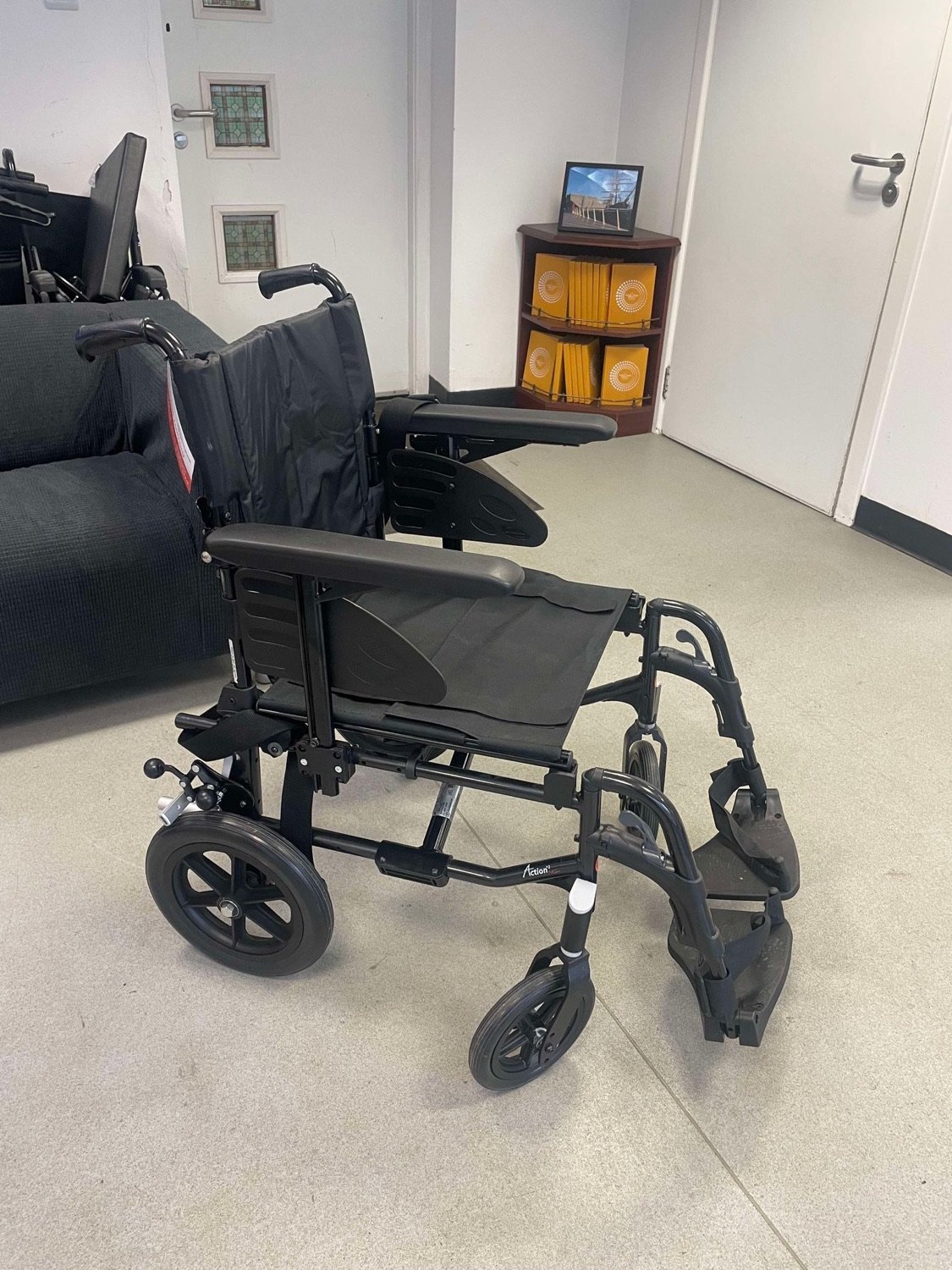 A black manual wheelchair, propelled by someone pushing from behind