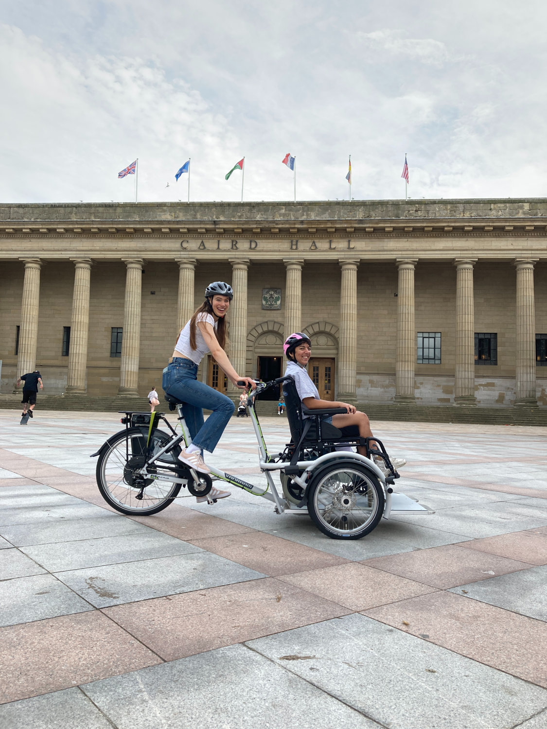 Two people riding the VeloPlus, a tricycle with a wheelchair platform at the front