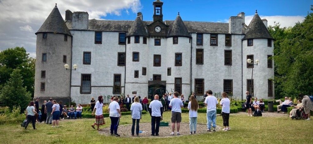 A photo of the front of Dudhope Castle, with groups of people standing in the garden in front of it. Some Uppertunity members are performing in front of the crowd