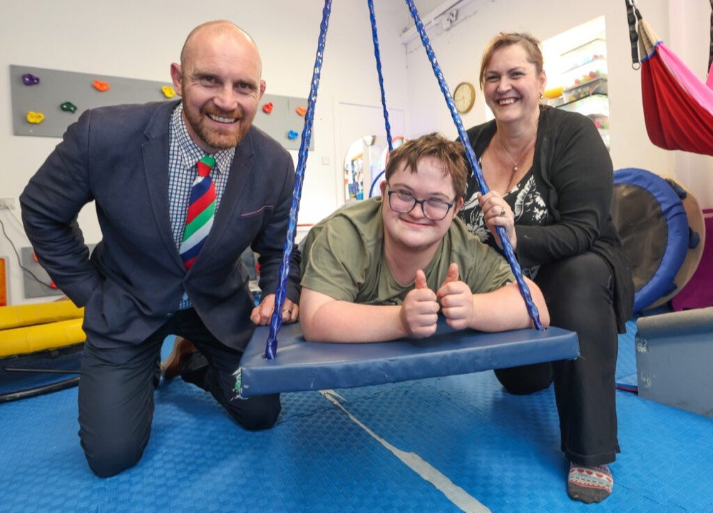A photo of Sharon Craighead, her son Sean and Al Kellock from Wooden Spoon charity. Sean is lying on a platform swing with Sharon and Al on either side of him