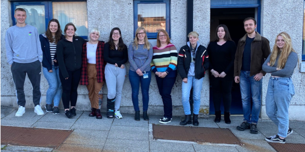 a group of people stand together in front of a grey building